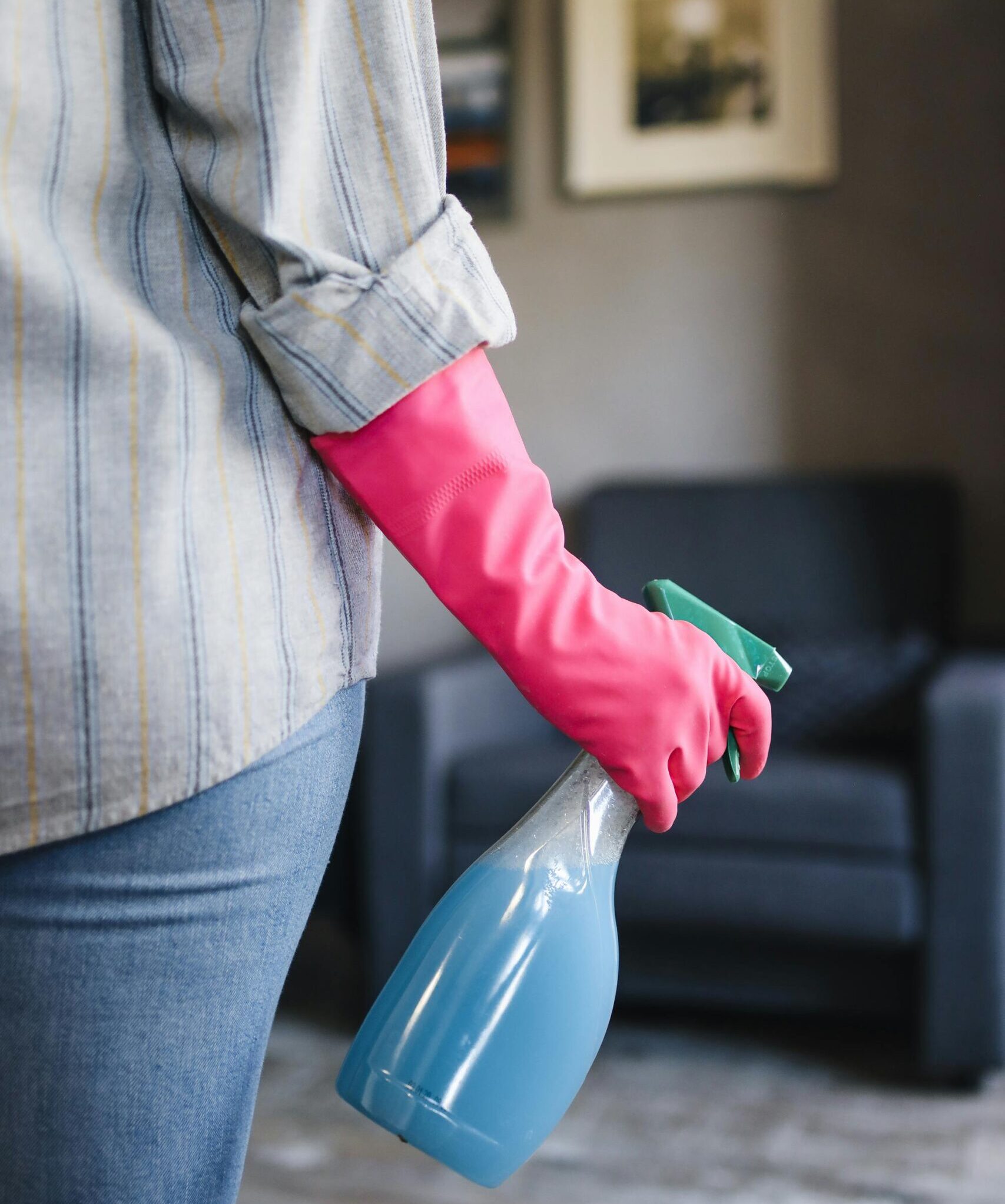 Close-up of a person in pink gloves holding a blue spray bottle indoors.